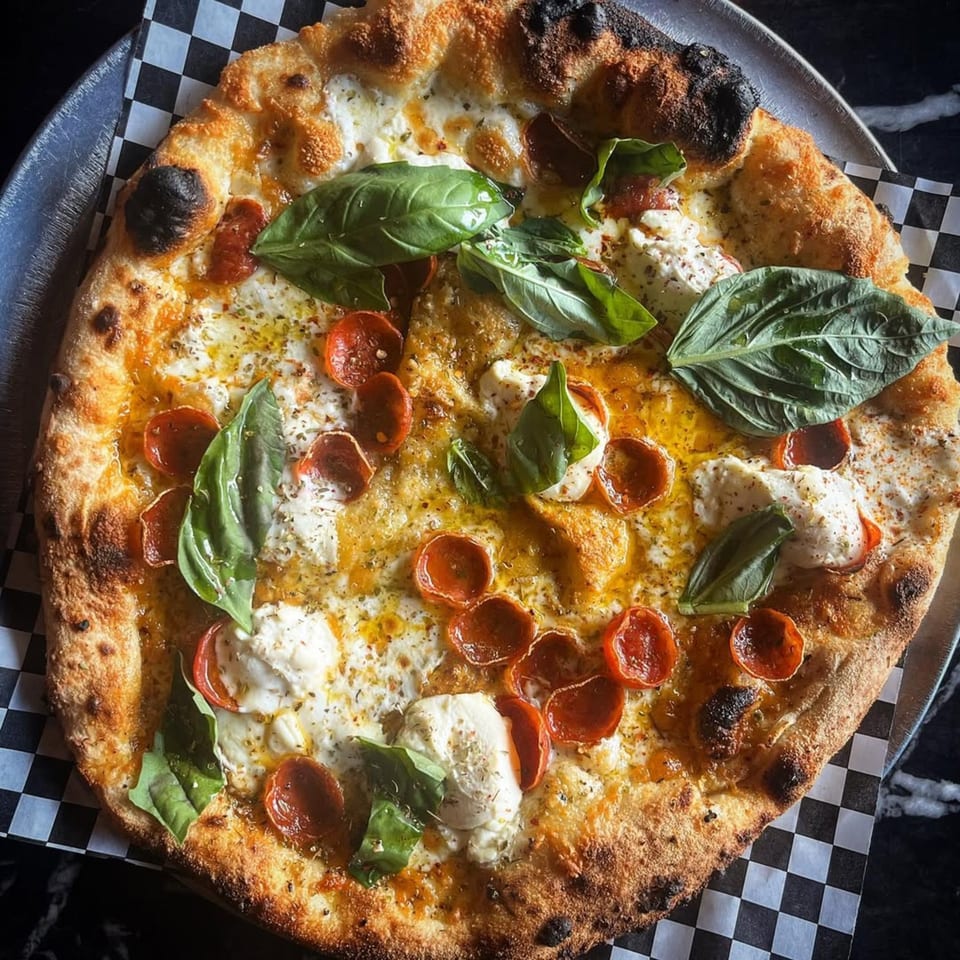 Coldpizza's pepperoni pizza with fresh basil, mozzarella, and olive oil on checkered paper.