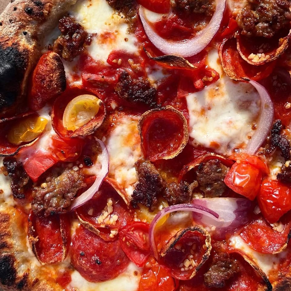 Coldpizza's pepperoni pizza with sausage, red onions, and roasted tomatoes, close-up.