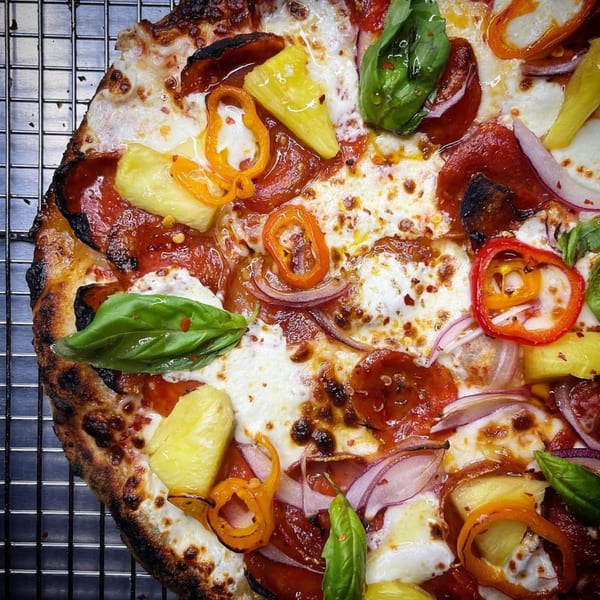 Coldpizza's pepperoni pizza with pineapple, red onion, bell peppers, and fresh basil on a cooling rack.