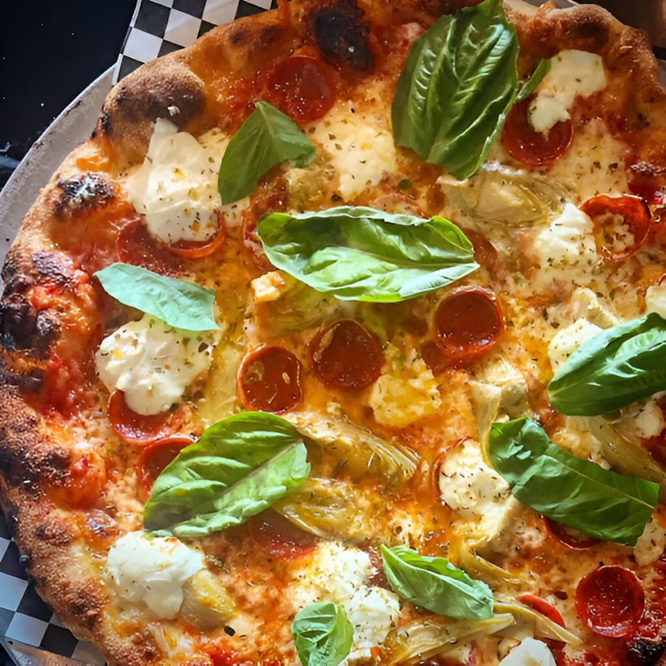 Coldpizza's pepperoni, artichoke, and fresh mozzarella pizza, garnished with basil leaves.