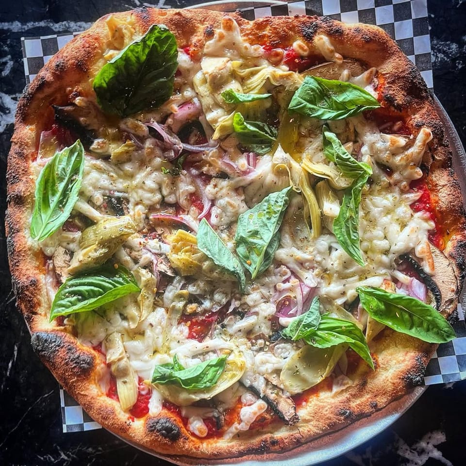 Coldpizza's wood-fired pizza with artichokes, red onion, mushrooms, melted cheese, and fresh basil.